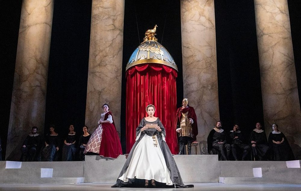 Cena de La Clemenza di Tito no palco, com o trono imperial, o elenco e a solista ao centro