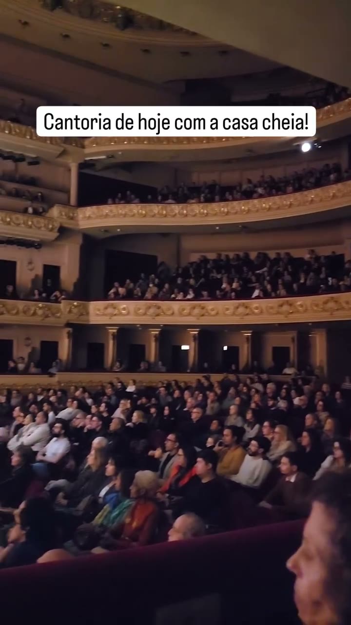 Plateia lotada em teatro durante uma apresentação, com todos os balcões ocupados